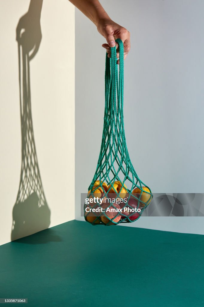 Still life of mesh shopping bag with organic eco vegetables and fruits on green background. Caring for the environment and the rejection of plastic concept