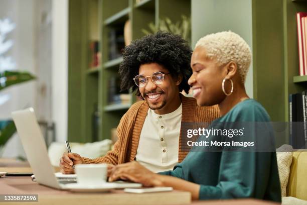 coworkers discussing over laptop at desk in office - black man laptop foto e immagini stock