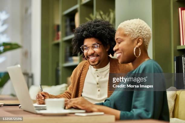 coworkers discussing over laptop at desk in office - african american businessman stock pictures, royalty-free photos & images