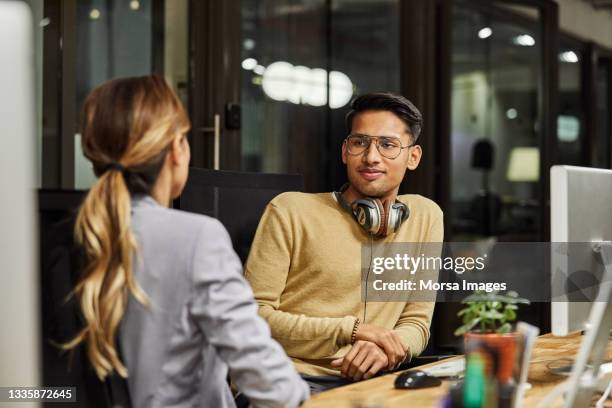 colleagues discussing at desk in creative office - night of empowering conversations stockfoto's en -beelden