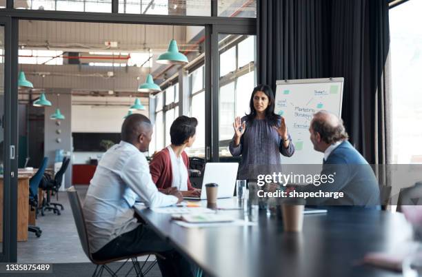 shot of a mature businesswoman using a whiteboard during a meeting with her colleagues in an office - director stockfoto's en -beelden