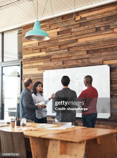 shot of a group of businesspeople brainstorming with notes on a whiteboard in an office - business strategy whiteboard stock pictures, royalty-free photos & images