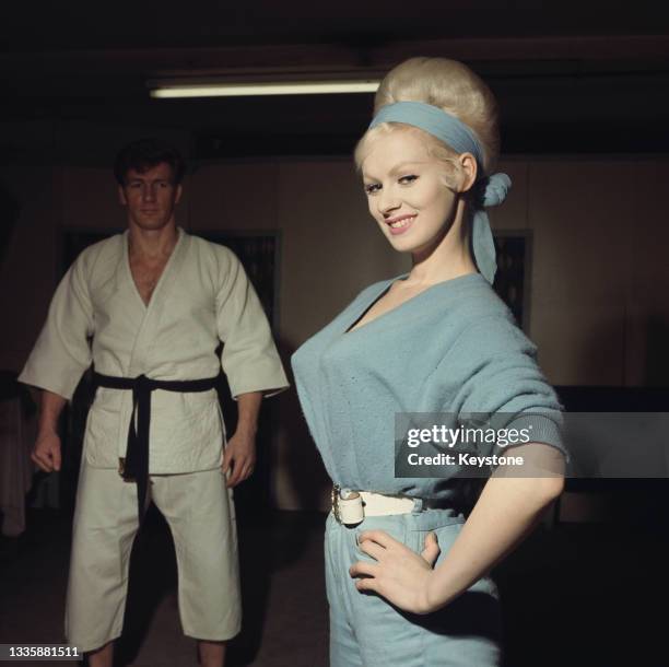 British glamour model and actress Sabrina , wearing a blue jumpsuit with matching headband, and British wrestler, martial artist and actor Joe...