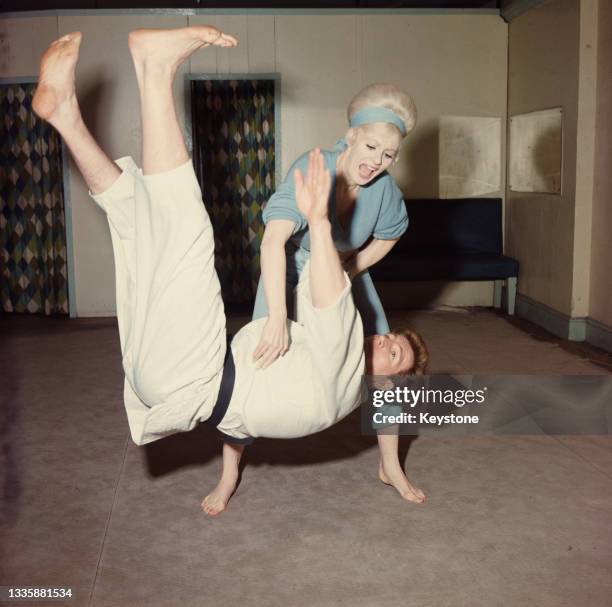 British glamour model and actress Sabrina , wearing a blue jumpsuit with matching headband, throws British wrestler, martial artist and actor Joe...