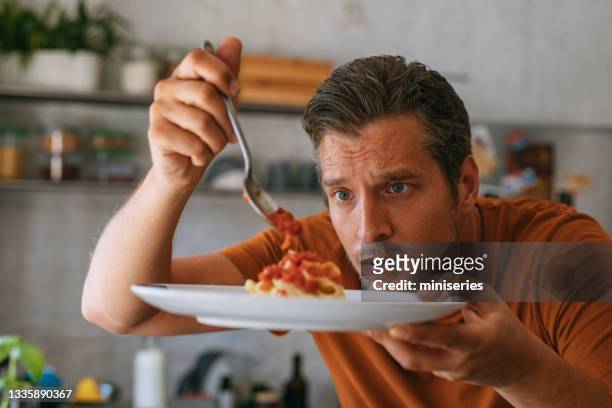 kochen zu hause: hübscher junger mann, der pasta zum abendessen macht - küche probieren stock-fotos und bilder