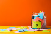 Colorful cards with question marks in glass jar on orange background. Space for text