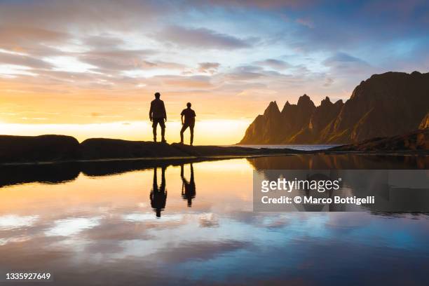 two people standing at the edge of a pond watching sunset in northern norway - 2 dramatic landscape stock pictures, royalty-free photos & images