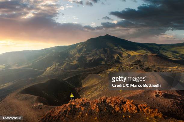 person standing on the edge of a volcanic crater at sunset - mt etna foto e immagini stock