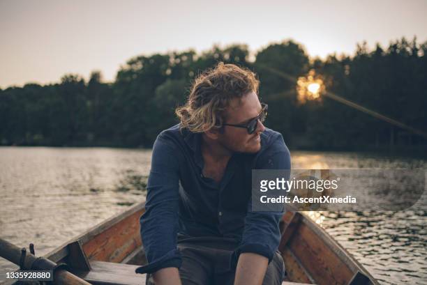 view of young man rowing boat down lakeshore - mid adult men stock pictures, royalty-free photos & images