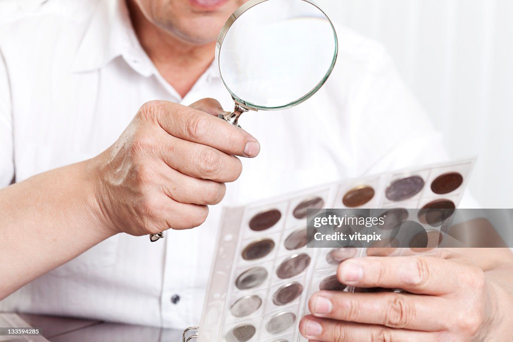 Mature man's hands holding a magnifying glass and coin collection