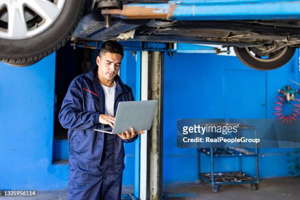 portrait of young mechanic using laptop in his auto repair shop - hanging board stock pictures, royalty-free photos & images