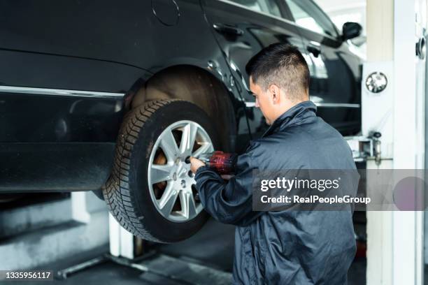 car service, repair and maintenance concept - auto mechanic man with electric screwdriver changing tire in auto repair shop. - tyre stockfoto's en -beelden