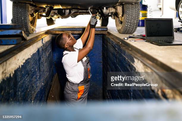 african woman as a mechatronics engineer in a car under repair in a car workshop - macacão preto imagens e fotografias de stock
