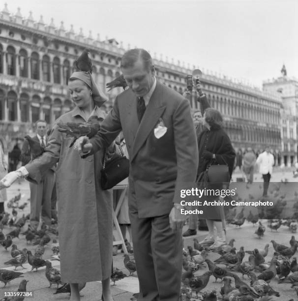 English actor Laurence Olivier with his wife Vivien Leigh portrayed while feeding pigeons in St. Mark Square, Venice, 1957.