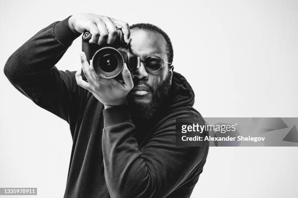 professioneller fotograf im studio, afroamerikaner tragen schwarzen kapuzenpullover und sonnenbrille mit digitalkamera funktioniert. schwarz-weiß-konzeptfotografie - photographer stock-fotos und bilder