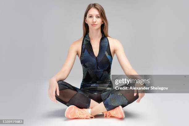 portrait of nice young woman in sportswear at the studio with gray background. concept with copy space. she is posing for camera. she have sports athletic body. girl sitting on the floor and smiling - lotus position imagens e fotografias de stock