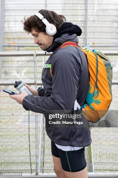 side view of male jogger in warm jacket and shorts with backpack standing in enclosed bridge with thermos bottle and cellphone in hands and looking away [ - running shorts foto e immagini stock