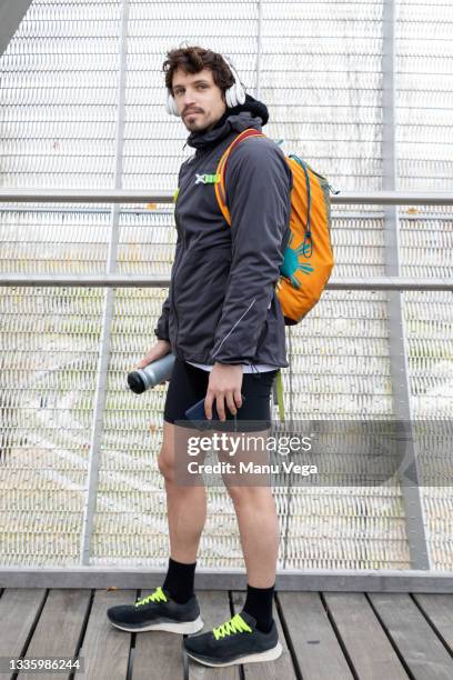 side view of male jogger in warm jacket and shorts with backpack standing in enclosed bridge with thermos bottle and cellphone in hands and looking at camera - running shorts foto e immagini stock
