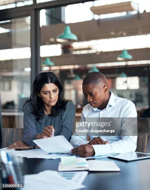 shot of a businessman and businesswoman going over paperwork in a modern office - asian and indian ethnicities imagens e fotografias de stock