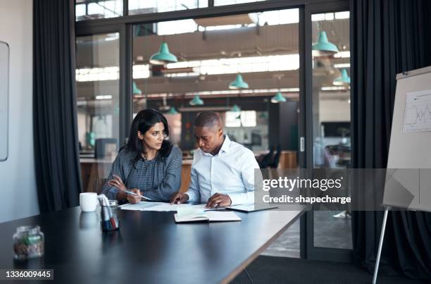 shot of a businessman and businesswoman going over paperwork in a modern office - indian college stockfoto's en -beelden