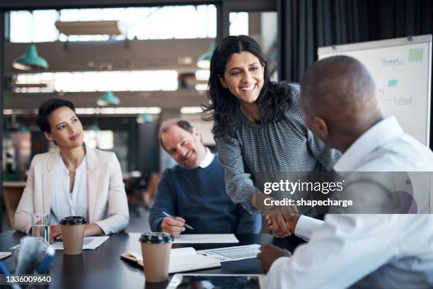 shot of a businesswoman and businessman shaking hands during a meeting in a modern office - woman-man-handshake-across-table stock pictures, royalty-free photos & images