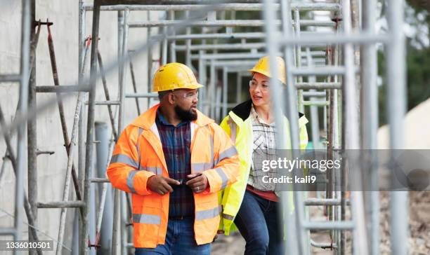 dos trabajadores de la construcción multiétnicos caminando, hablando - scaffolding fotografías e imágenes de stock