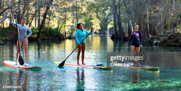 three women side by side paddle boarding on river, laugh - paddleboarding 個照片及圖片檔