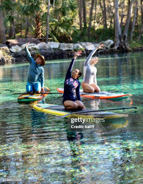 drei personen praktizieren yoga auf paddleboards auf dem fluss - fersensitz stock-fotos und bilder