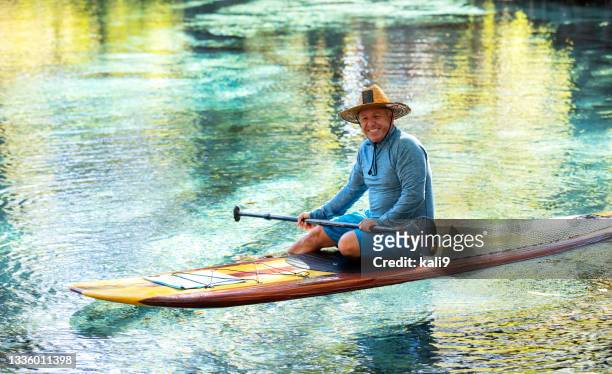 hombre maduro sentado en la tabla de paddle, sonriendo a la cámara - long sleeved fotografías e imágenes de stock