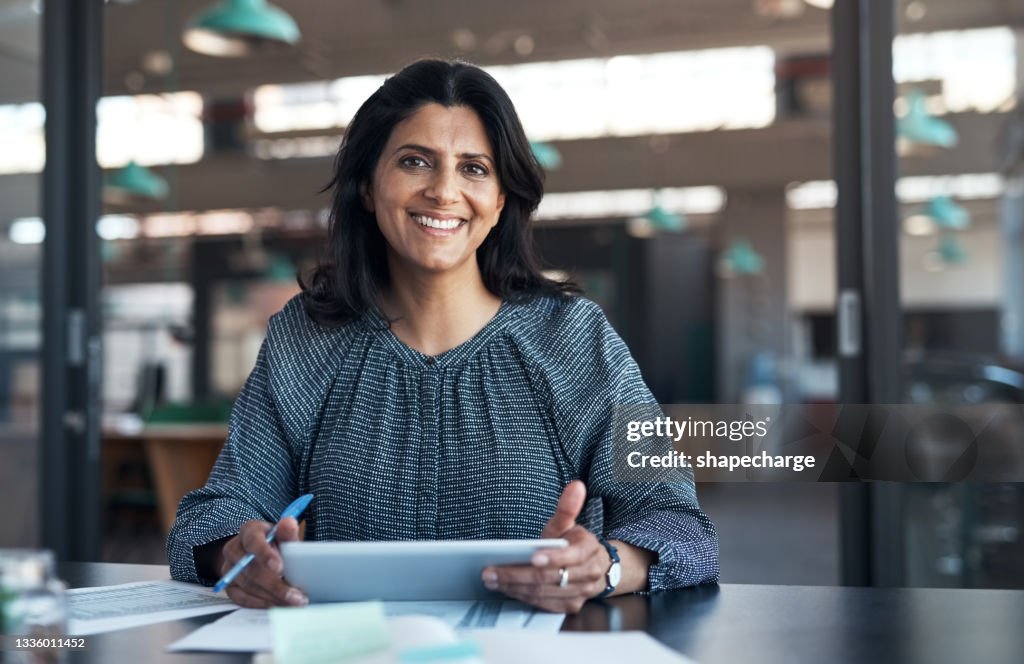 Aufnahme einer reifen Geschäftsfrau, die ein digitales Tablet verwendet und in einem modernen Büro Papierkram durchläuft
