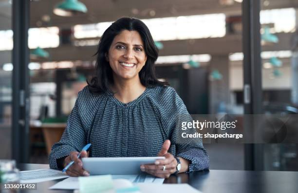 shot of a mature businesswoman using a digital tablet and going through paperwork in a modern office - asian and indian ethnicities imagens e fotografias de stock