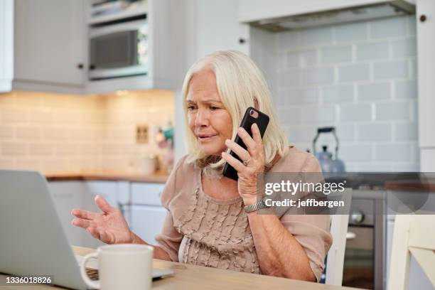 shot of a senior woman looking angry while using a smartphone and laptop at home - frustrated stock pictures, royalty-free photos & images