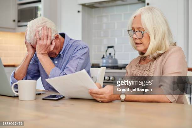 shot of a senior couple looking unhappy while going through paperwork at home - erfenis stockfoto's en -beelden