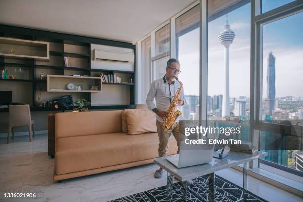 ライフハックアジアのアクティブなシニアマンアーティストは、サックスを演奏し、市内のアパートのリビングルームでラップトップを使用して彼の学生にそれを示しています - jazz showcase ストックフォトと画像