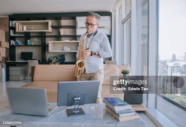 asian chinesse active senior man artist playing saxophone and showing it to his student using laptop at apartment living room in city live streaming - lifehack stockfoto's en -beelden