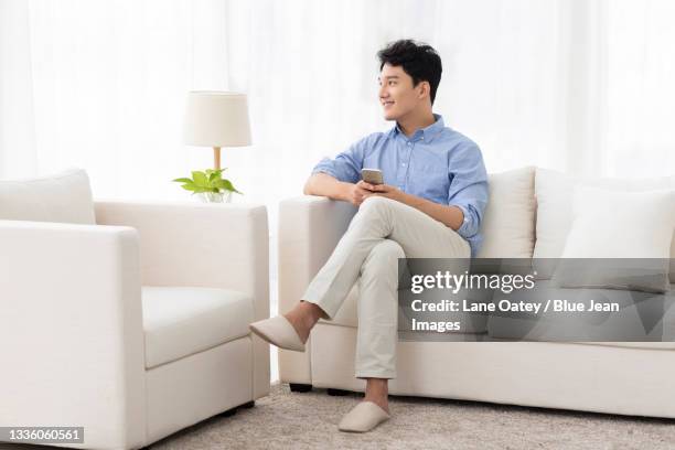 cheerful young man sitting on sofa - man sitting on sofa fotografías e imágenes de stock