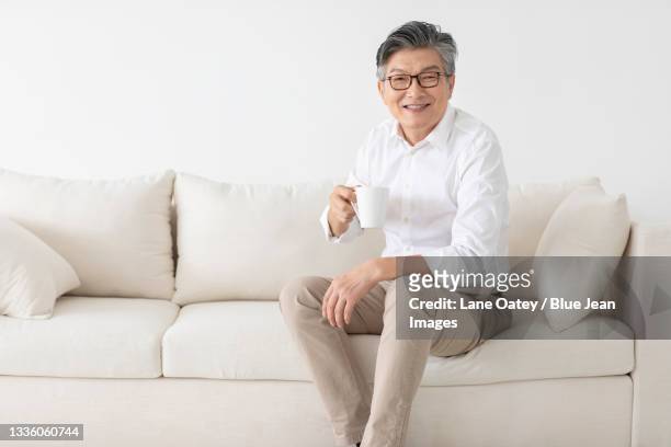 cheerful senior chinese man drinking coffee at home - three quarter length stock pictures, royalty-free photos & images