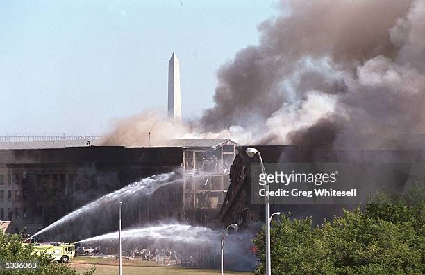 The Washington Momument stands in the background as firefighters pour water on a fire at the Pentagon that was caused by a hijacked plane crashing...