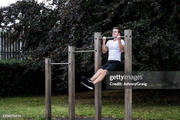 engagierter junger mann, der bei regenwetter klimmzüge im park macht - gym equipment stock-fotos und bilder