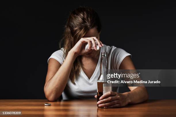 young drunk woman crying while drinking a bottle of beer alone in a bar. - alcolismo foto e immagini stock