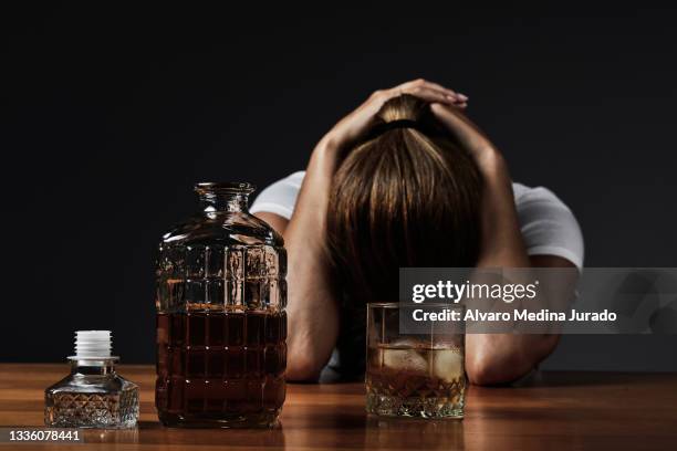 young depressed drunk woman with hands on head while drinking whiskey alone in a bar. - alcoholic stock-fotos und bilder