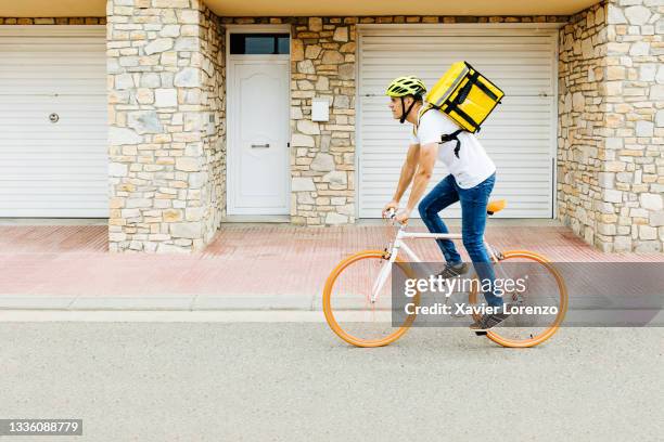 courier hispanic man doing fast food delivery with thermal backpack riding trendy bicycle - delivery bike stock-fotos und bilder