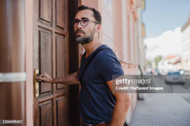 mature happy man standing in town street, opening door of building. - entering building stock pictures, royalty-free photos & images