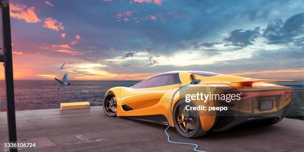 gelber elektrischer sportwagen, der vom kabel auf dem parkplatz mit blick auf das meer im morgengrauen aufgeladen wird - luxury car stock-fotos und bilder