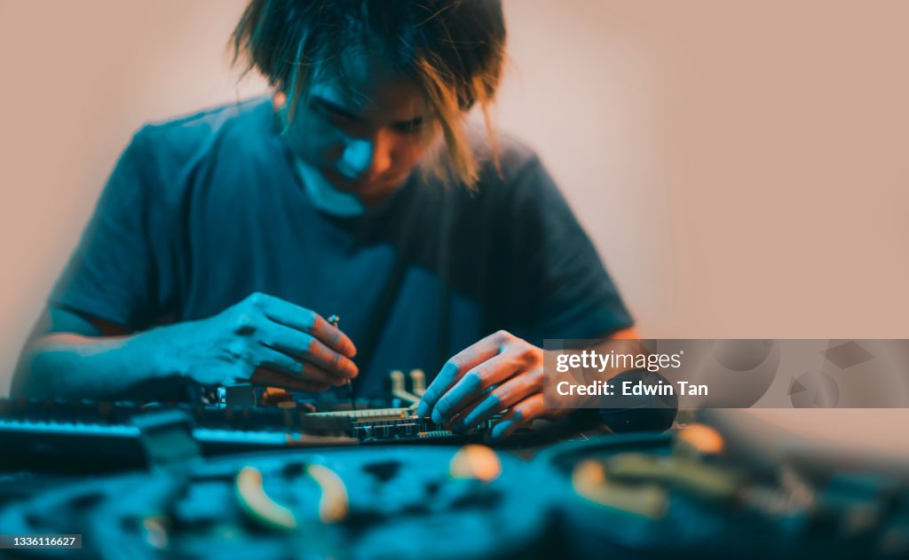 Asian chinese teenage boy repairing computer motherboard with work tool diagnosis tighten at night at home