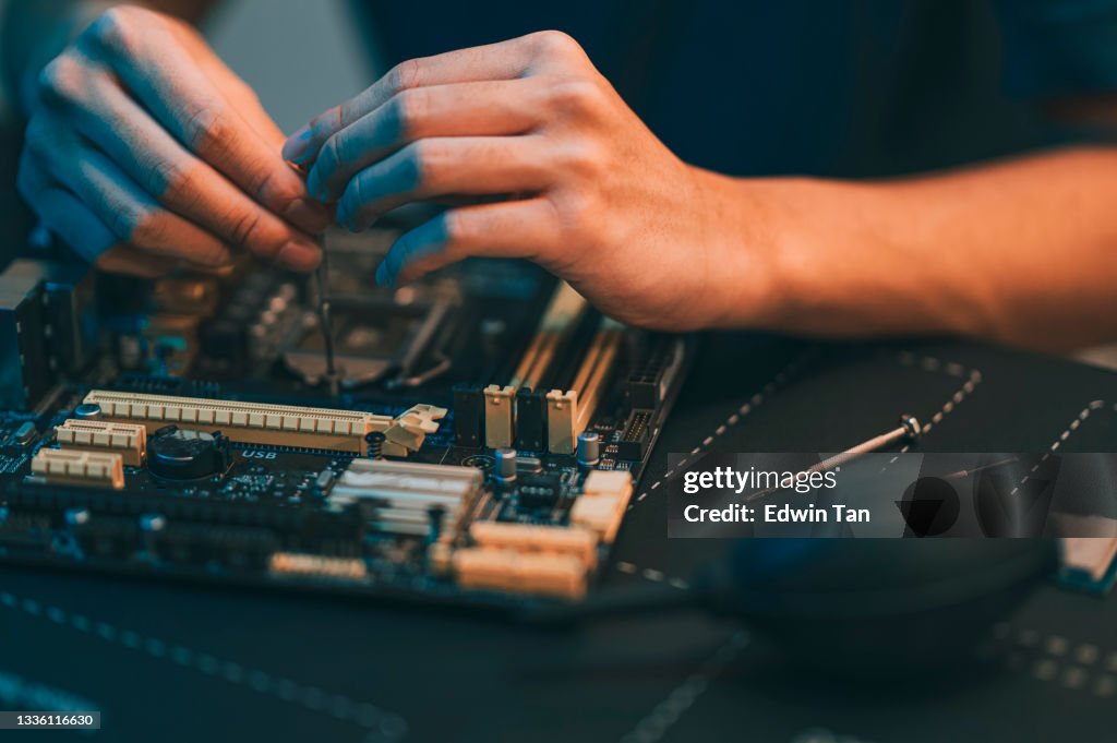 Asian chinese teenage boy repairing computer motherboard with work tool diagnosis tighten at night at home