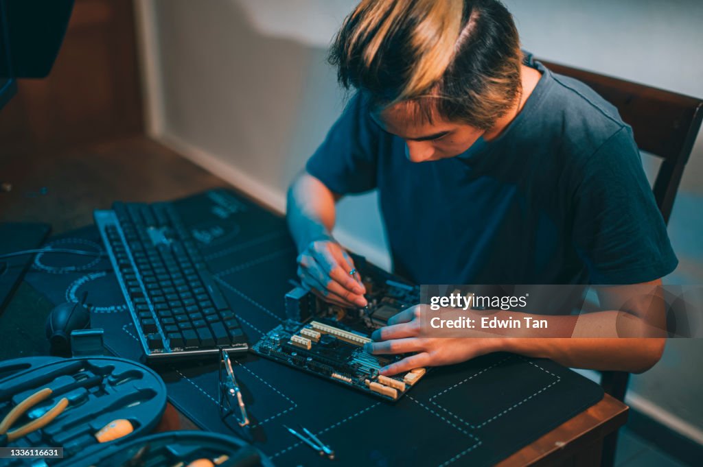 Asian chinese teenage boy repairing computer motherboard with work tool diagnosis tighten at night at home