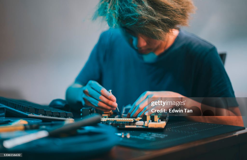 Asian chinese teenage boy repairing computer motherboard with work tool diagnosis tighten at night at home