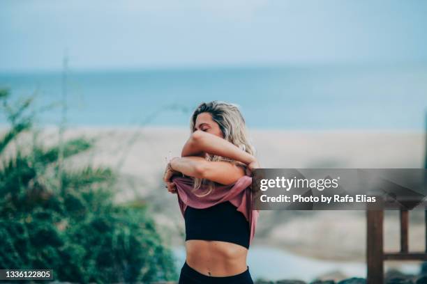 woman taking off t-shirt on the beach promenade - entkleiden stock-fotos und bilder