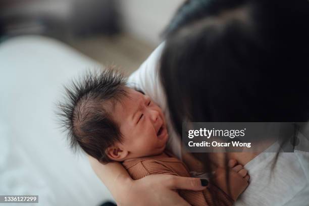 young mother comforting crying baby daughter in her arms - moms crying in bed stockfoto's en -beelden